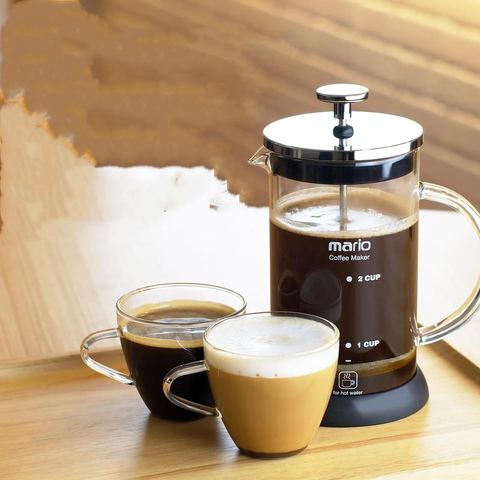 French press coffee maker with two cups of coffee on a wooden surface